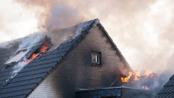Fragment of a sooty white brick home that is on fire with flames and smoke cming out stock photo