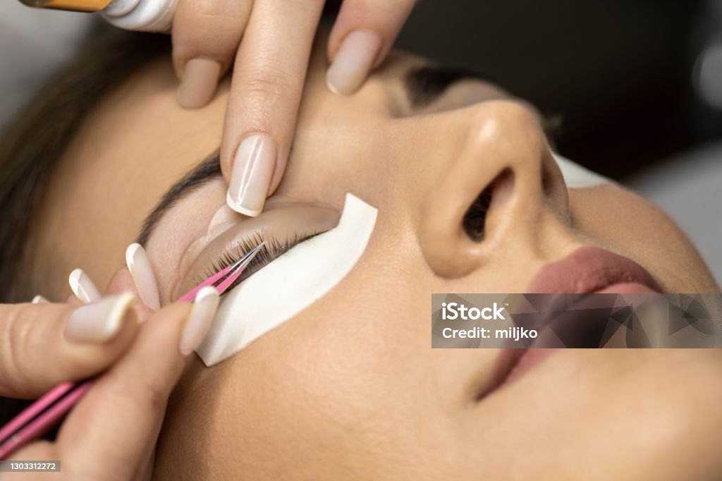 Lash lamination treatment in the salon Beautiful young woman with beautiful clean skin having a lash lift treatment. She is laying on the bed, her eyes are closed and the beautician is doing the treatment. Eyelash Stock Photo
