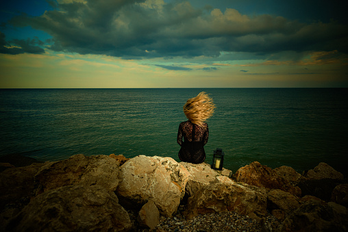 Rear view of blond woman with blond hair in the air feeling relaxed but lonely at the sea