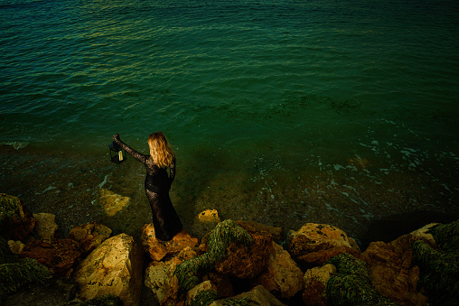 High angle view of blond woman wearing black dress posing with lantern at the sea in Romania