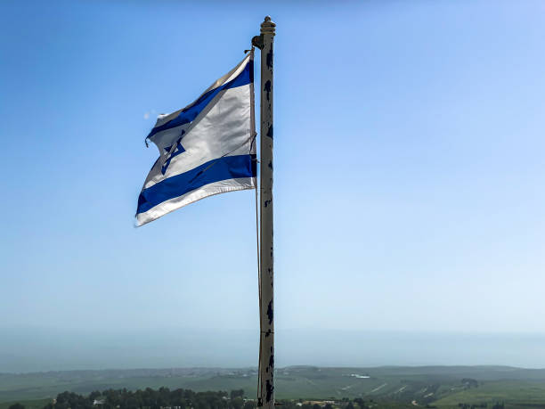 istock Partially torn israeli flag is waving in the wind on blue sky background 1303319790