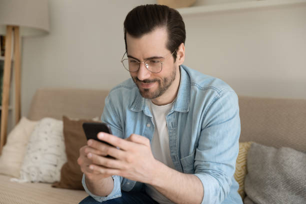 istock Positive millennial man resting on sofa at home using phone 1303320159