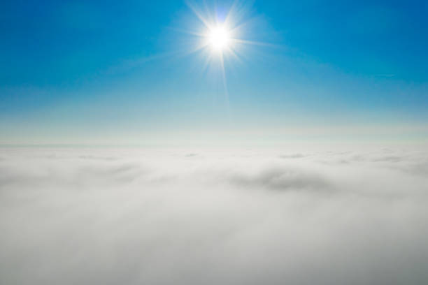 Panoramic view of sun rays shining in the blue sky above white and fluffy clouds.