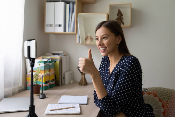 istock Woman student finishing task showing thumb up to phone webcam 1303320233