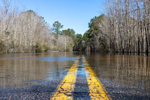 River water washes over a road during a spring flood. Low angle centered wide shot over yellow dividing lines.