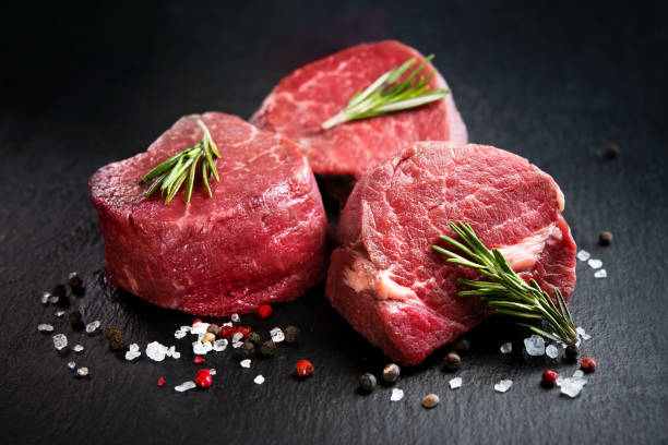 Raw beef filet mignon steaks with rosemary, pepper and salt on dark rustic board Raw beef filet mignon steaks with rosemary, pepper and salt on dark rustic board, black angus meat beef stock pictures, royalty-free photos & images