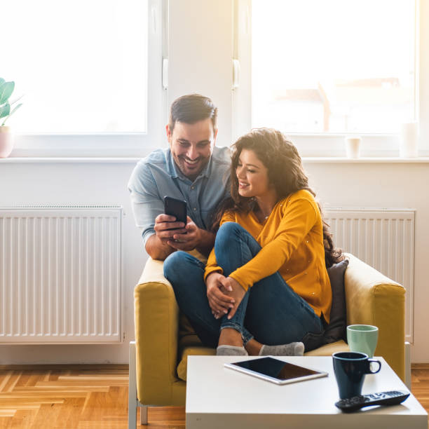 istock Smiling couple looking in smartphone together at home 1303326109