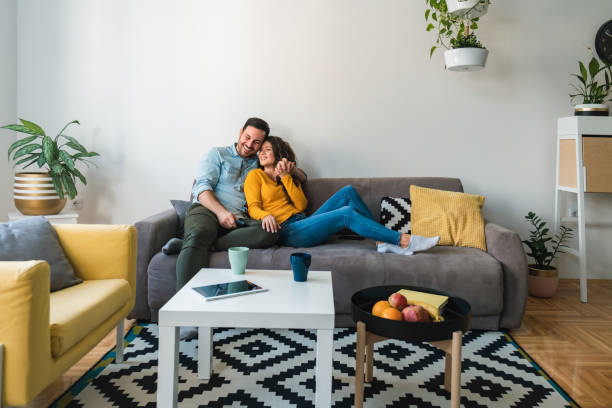 pareja abrazada relajándose juntos en su sofá en la sala de estar en casa - pareja de mediana edad fotografías e imágenes de stock
