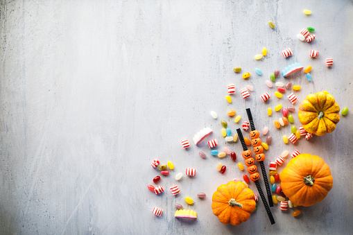 Flat lay of colorful candy, fun Jack o' lantern drinking straws and gourds in a bottom right corner of a shot on a white background with copy space in the middle.