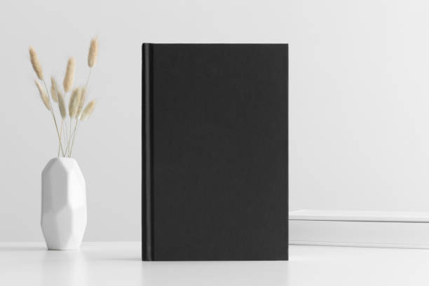 istock Black book mockup with a lagurus and workspace accessories on a white table. 1303331565