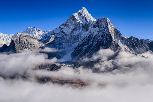 Panorama of Mount Ama Dablam - probably the most beautiful peak in Himalayas. \nAma Dablam is a mountain in the Himalaya range of eastern Nepal. The main peak is 6,812  metres, the lower western peak is 5,563 metres. Ama Dablam means  'Mother's neclace'; the long ridges on each side like the arms of a mother (ama) protecting  her child, and the hanging glacier thought of as the dablam, the traditional double-pendant  containing pictures of the gods, worn by Sherpa women. For several days, Ama Dablam dominates  the eastern sky for anyone trekking to Mount Everest basecamp