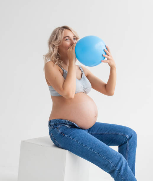 una hermosa joven embarazada con un gran vientre en jeans azules sostiene un globo que significa que un niño nacerá. - balloon blowing inflating child fotografías e imágenes de stock