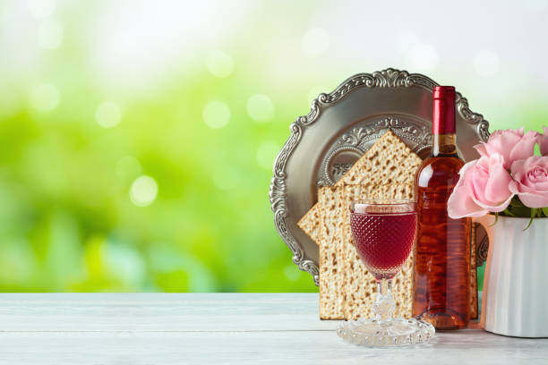 concepto de pascua de vacaciones judías con vino, matzah, flores y placa de seder sobre mesa de madera sobre fondo bokeh verde - passover matzo seder spring fotografías e imágenes de stock