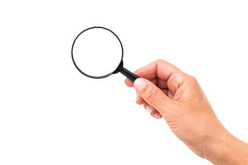 Close up view of a female hand holding a magnifying glass isolated on white background. Copy space. High resolution 42Mp studio digital capture taken with Sony A7rII and Sony FE 90mm f2.8 macro G OSS lens