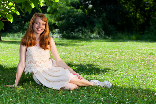 Summer portrait of young attractive woman outdoors. She is sitting on grass and smiling into the camera. Shallow DOF.