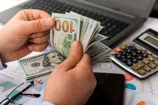 Businessman counting hundreds of dollars at his table