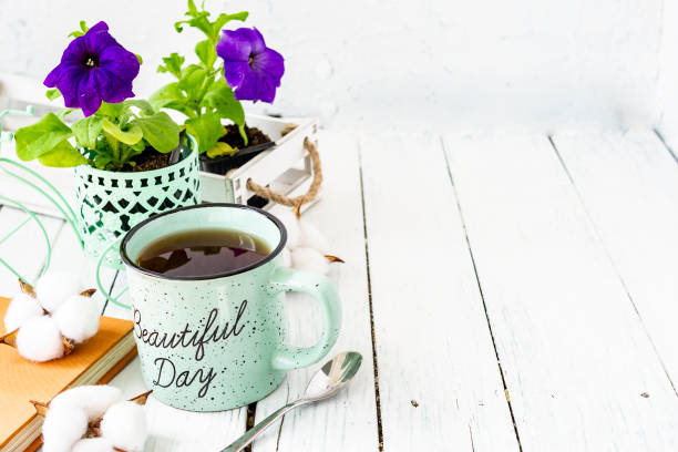 Close-up of a cup of tea on a wooden white table with blurred background, front blur. Still life with flower, book, teaspoon, cotton box. Spring breakfast. Copy space. Close-up of a cup of tea on a wooden white table with blurred background, front blur. Still life with flower, book, teaspoon, cotton box. Spring breakfast. Copy space tea party horizontal nobody indoors stock pictures, royalty-free photos & images