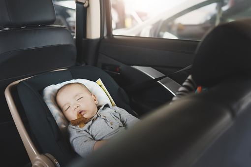Cute Asian newborn baby boy with pacifier sleeping on his car safety seat in car while traveling.