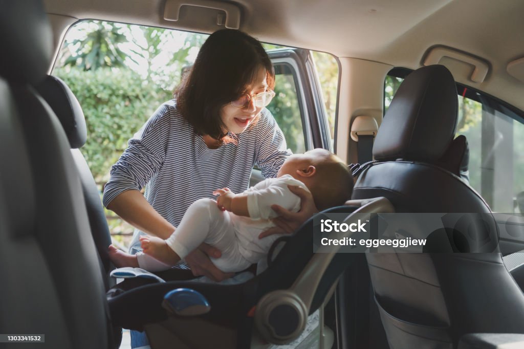 Asian young mother putting her baby son into car seat Asian young mother putting her baby son into car seat and fasten seat belts in the car for safety in transportation. Car Safety Seat Stock Photo