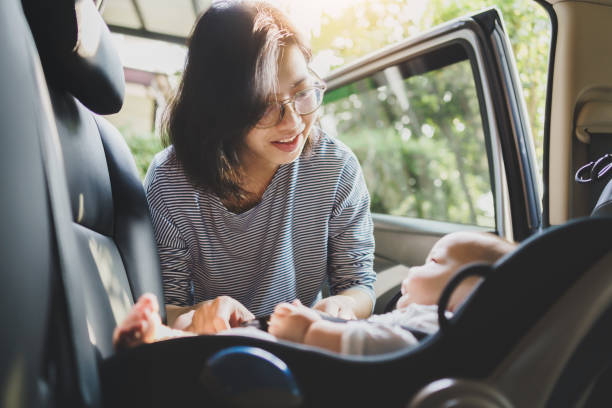 felice sorridente madre asiatica che aiuta il suo figlio piccolo a fissare la cintura sul sedile dell'auto in auto per la sicurezza nei trasporti - asian ethnicity baby mother family foto e immagini stock