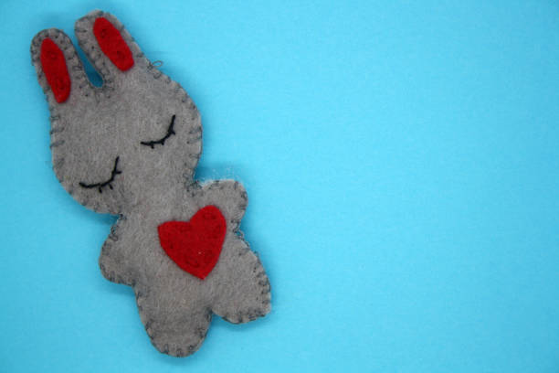 A bunny made of gray felt with a red heart. Space for text.