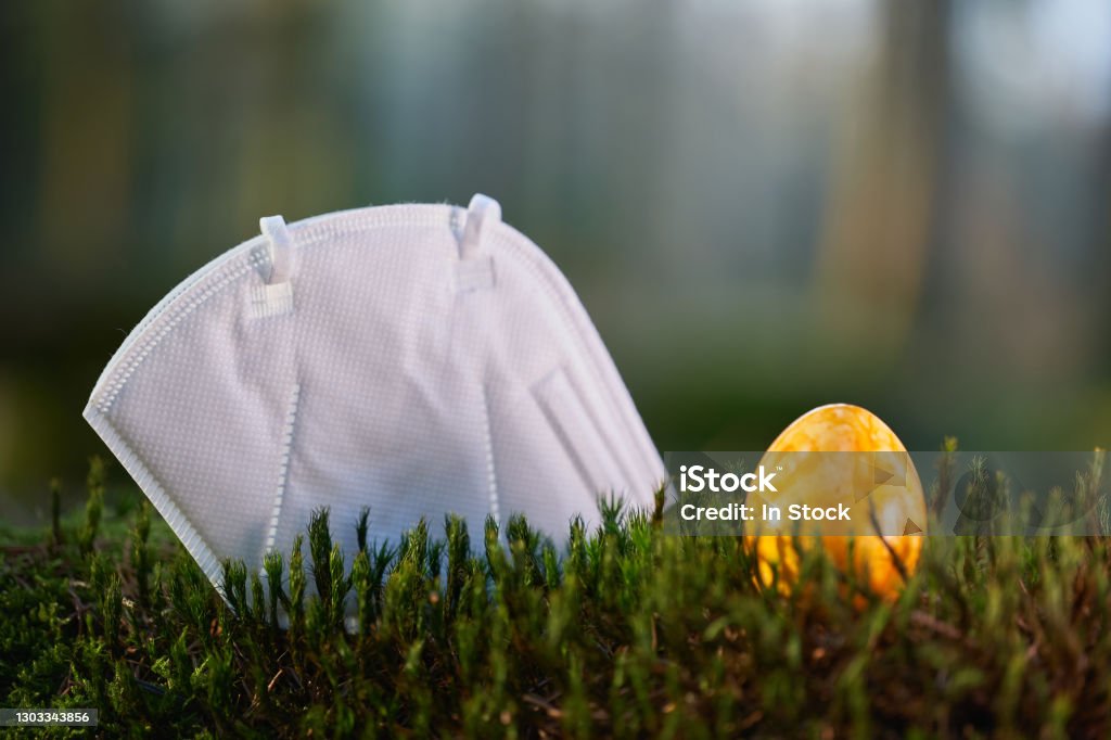 Fpp2 Face Mask on a mossy ground in the forest, yellow easter egg. FFP2 Mask Stock Photo
