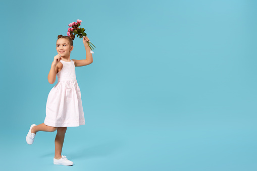 happy little girl holds bouquet of roses and runs isolated on blue studio background. Copy space