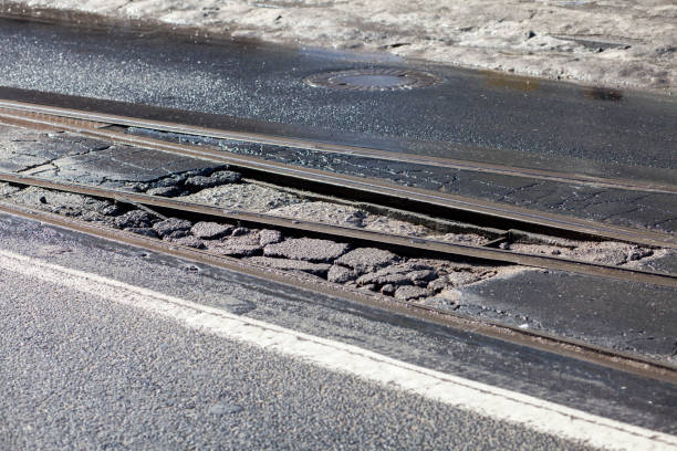 на улице между трассами из-за зимних погодных условий создана яма - pot hole street car hole стоковые фото и изображения