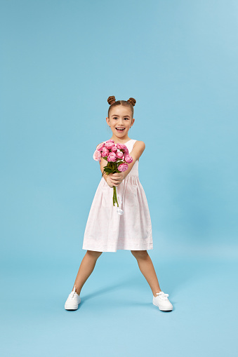 very excited smiling little girl holding bouquet of roses isolated on blue studio background. child gives bouquet to mom. mothers day