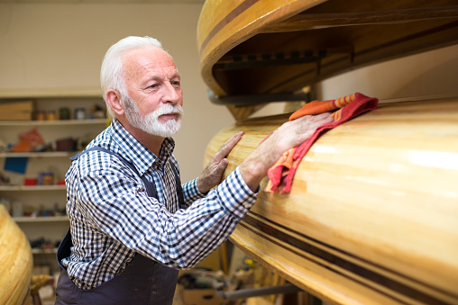 Senior man carpenter polishing wooden canoe in his workshop.