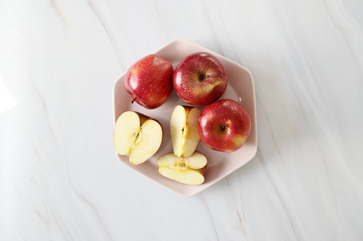 Istanbul, Turkey-February 21, 2021: Red Ripe Whole Apples and Apple Slices on a Powder Pink Hexagonal Plate on a White Marble Background. Full Frame, Still life, Studio shot, Flat lay. Shot with Canon EOS R5, Canon RF 35mm Lens.