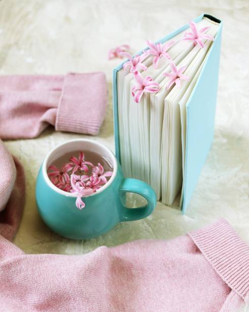 Cup with a drink, fresh flowers bookmarks in an open book, woolen pink sweater on a light background