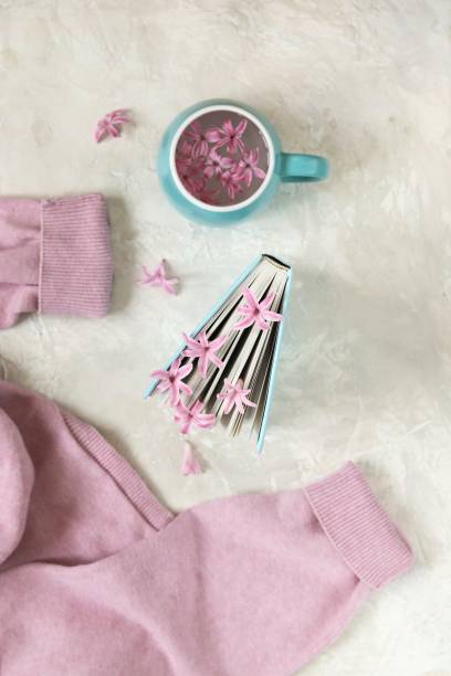Cup with a drink, fresh flowers bookmarks in an open book, woolen pink sweater on a light background