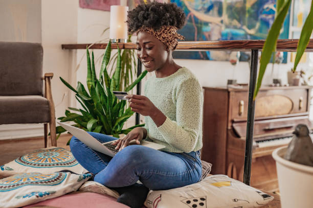 Online shopping from home A young woman is in the living room, she is using a laptop and credit card financial wellbeing stock pictures, royalty-free photos & images