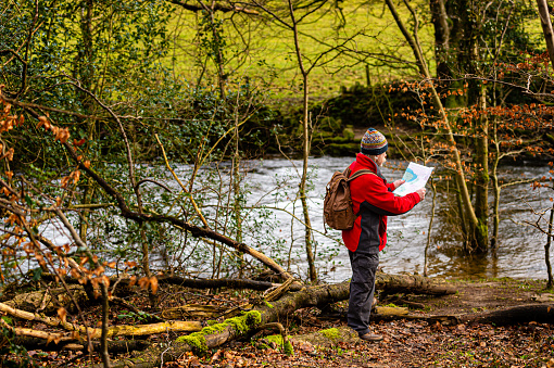 A senior man looking at his map as he stands beside a small river