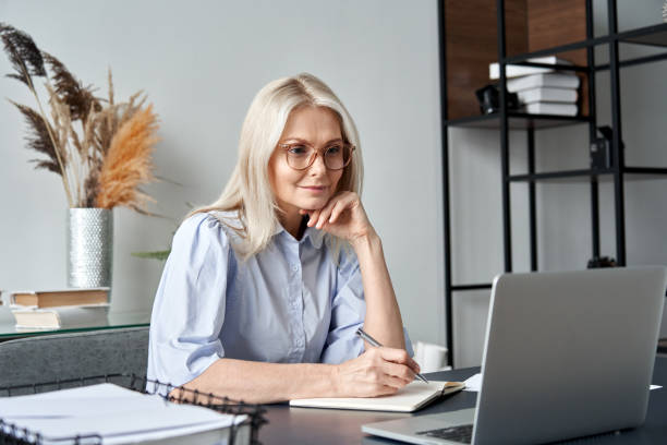 istock Middle aged older business woman watching professional training class, online webinar on laptop computer remote working, distance learning from home office, conference calling in virtual chat meeting. 1303367756