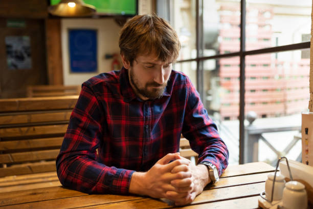 istock Sad young man sitting alone at a table in a bar. Alcohol addiction concept. 1303374026
