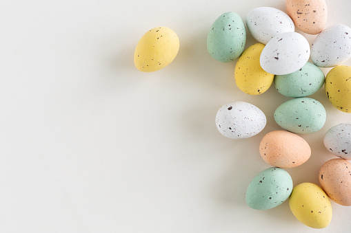A beautiful spread of chocolate easter egg in pastel colors on the right on a white background, flat lay with copy space