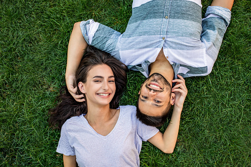 Portrait of young man and woman lying on the grass, looking at camera and smiling