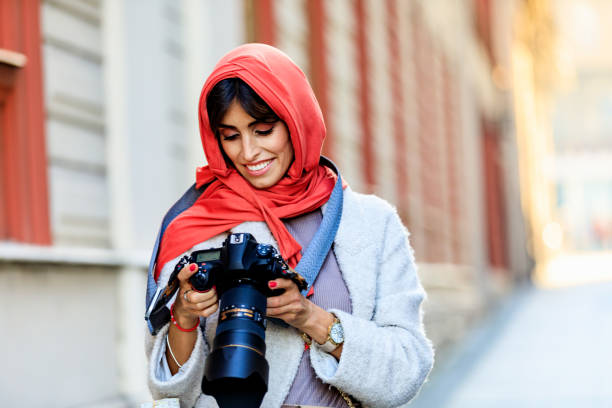 Arab Female photographer takes a photo with a digital camera. A Mature Muslim Woman photographing you with a camera. Photographer with a lens in his hand on a city street.