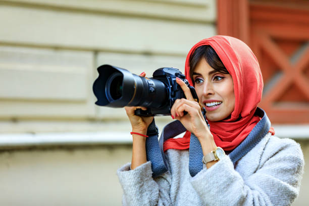 Arab Female photographer takes a photo with a digital camera. A Mature Muslim Woman photographing you with a camera. Photographer with a lens in his hand on a city street.