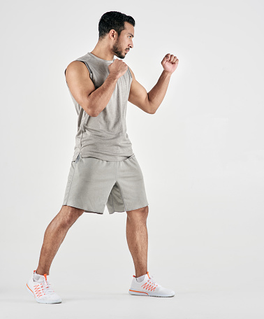 Studio shot of a muscular young man posing in fighting stance against a white background