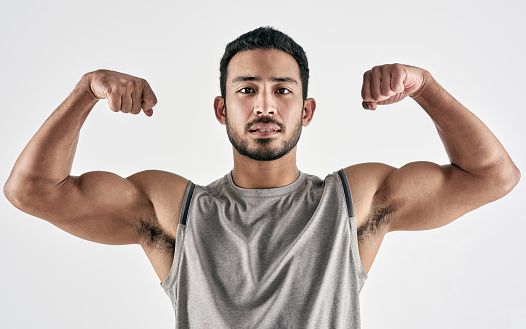 Studio portrait of a muscular young man flexing his biceps against a white background