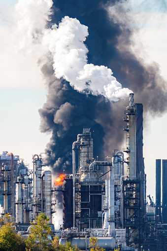 Fire and black smoke at an oil refinery after an explosion. Towers visible in front of smoke and flame. Scene slightly blurred due to volatile air.