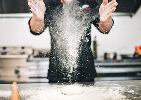 Chef baker preparing a pizza in the italian restaurant. He use fresh products, and throwing flour in the air