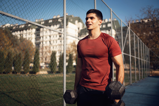 Young man doing alternating dumbbell curls exercise outside.