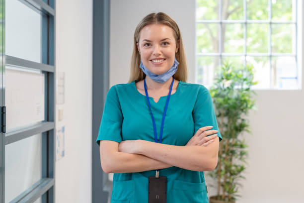 Portrait of smiling healthcare worker on break between seeing patients A female nurse smiles directly at the camera while on break between patients, with protective face mask pulled down below her chin. self sacrifice stock pictures, royalty-free photos & images