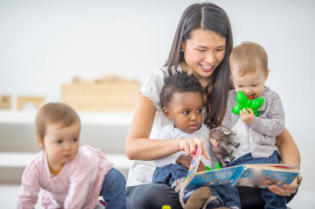 Preschool teacher reads a book to her students A female Asian preschool teacher is reading a book to her group of children. child care stock pictures, royalty-free photos & images