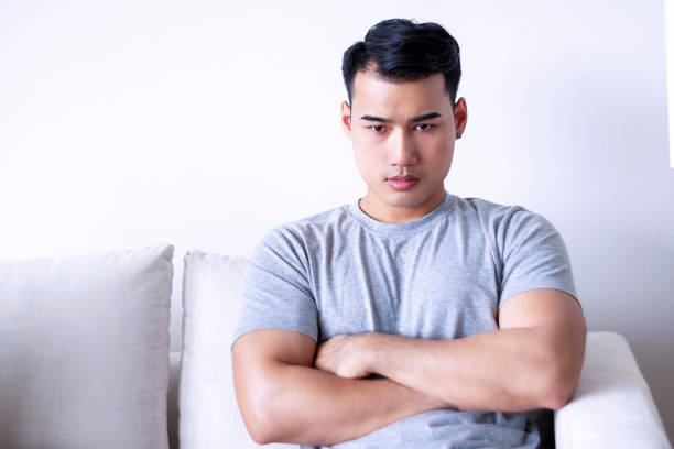 um jovem deprimido ou infeliz que teve problemas enquanto senta no sofá lamenta sua culpa em casa. homem cansado pensando em algo enquanto senta no sofá sozinho na sala de estar. - portrait male pensive sofa - fotografias e filmes do acervo