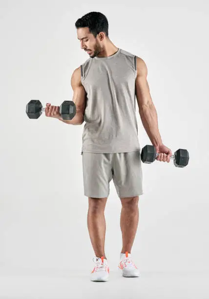 Studio shot of a muscular young man exercising with dumbbells against a white background